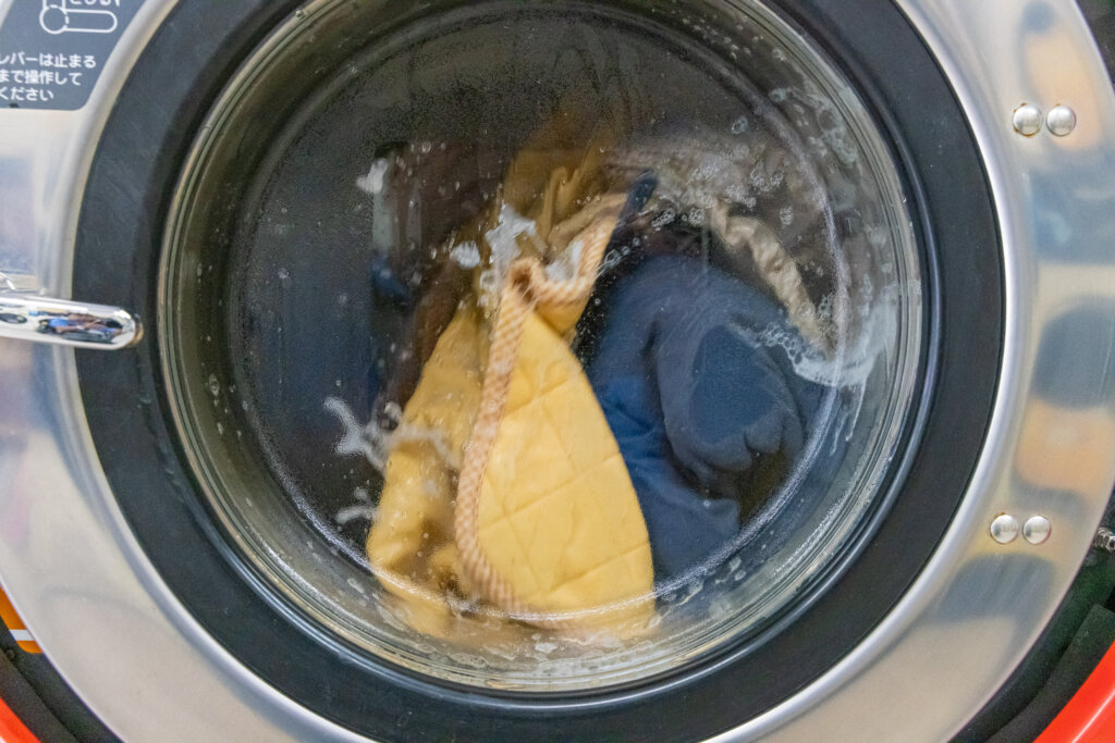 業務用洗濯機の中で作業着が泡立ちとともに洗濯されている様子