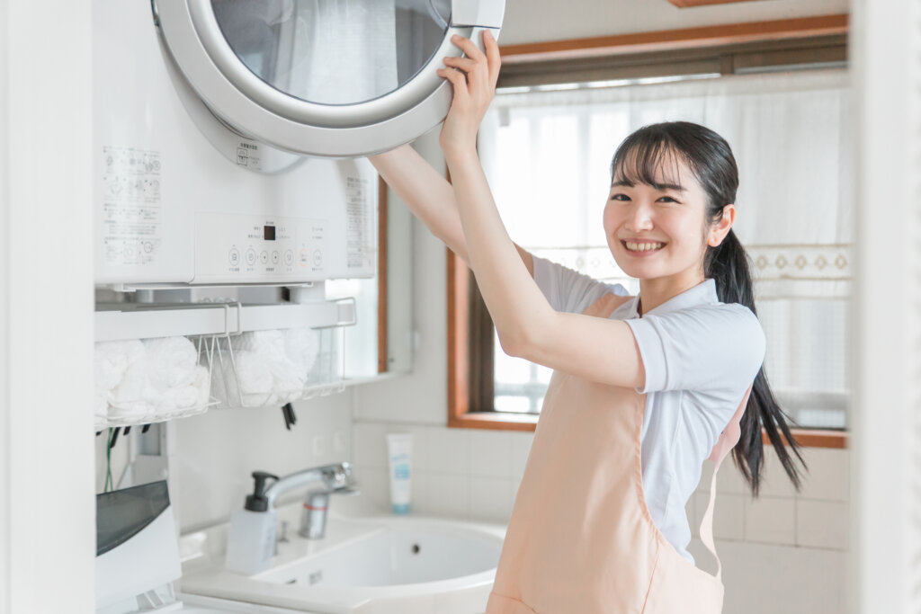 業務用洗濯機にタオルを入れる女性スタッフの笑顔