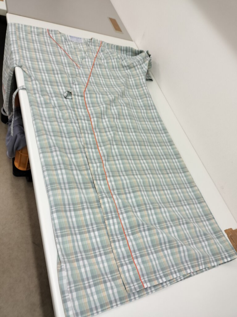 患者衣を広げた状態。チェック柄が整ったまま台の上に平置きされている。
