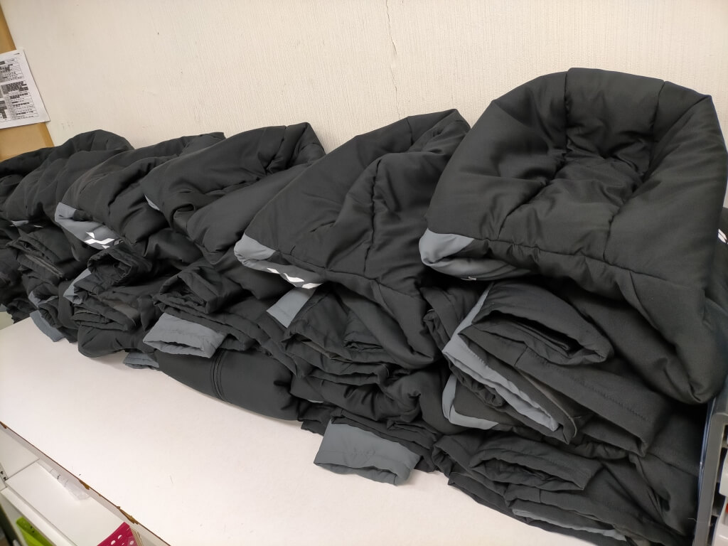 洗濯と乾燥を終えた黒いベンチコートが綺麗に整列して積まれている様子