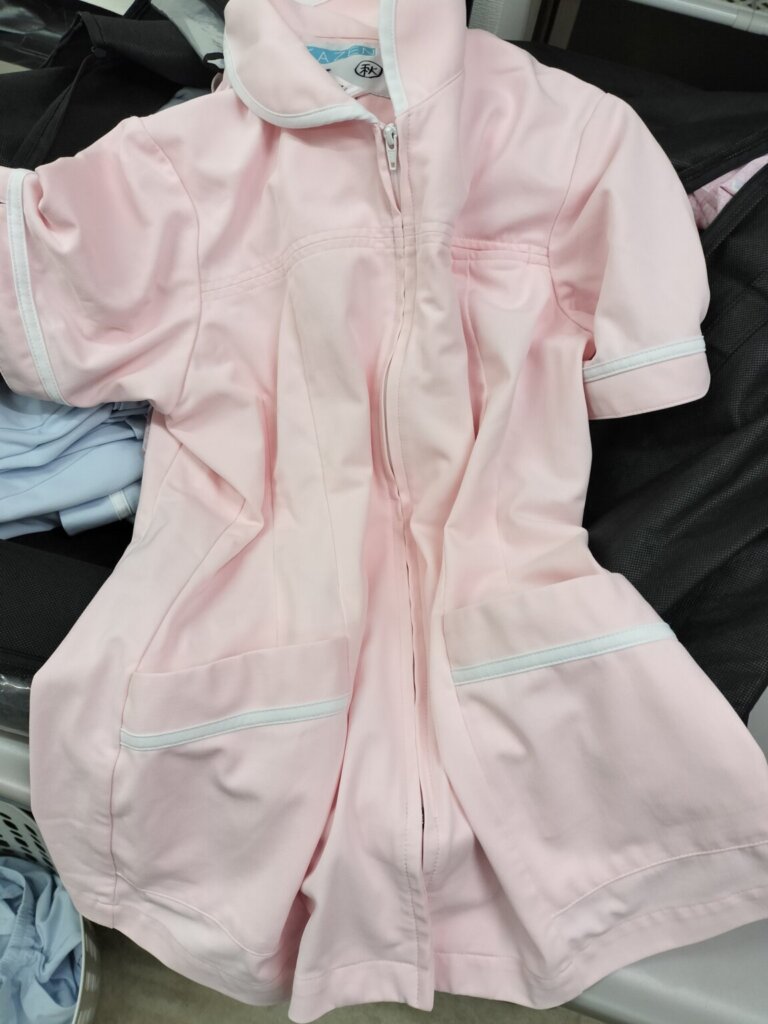 洗濯前のピンク色の看護師白衣を検品している様子